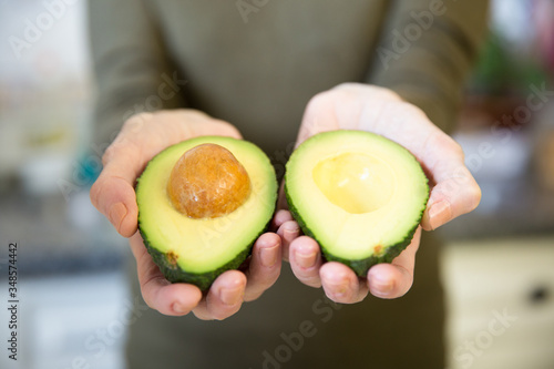 Woman showing avocado cut halves at camera in outstretched hands. Closeup shot. Unrecognizable person cooking in her kitchen. Fresh food or staying at home concept