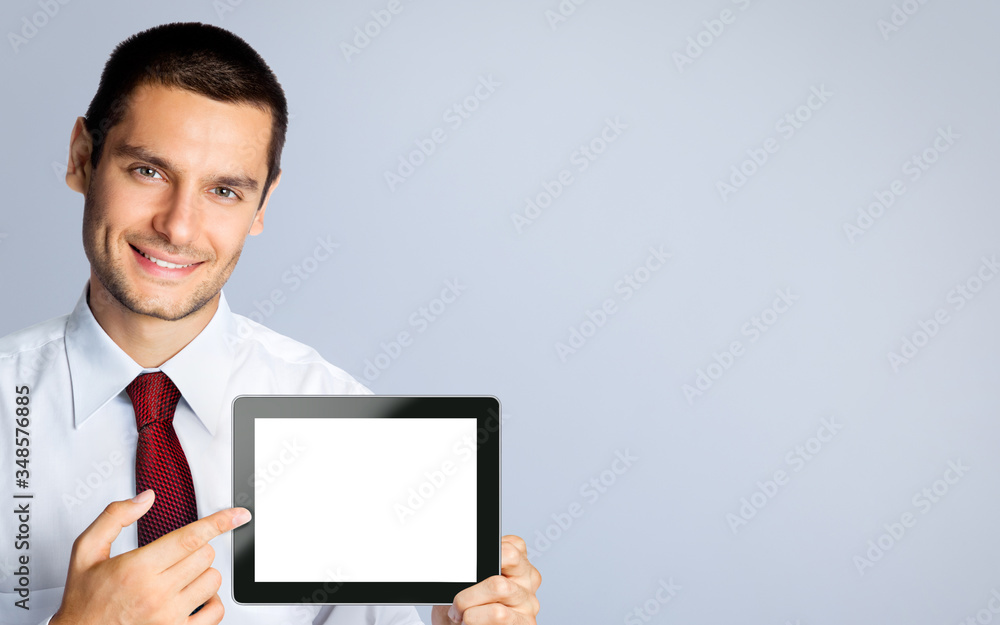 Cheerful confident businessman in white shirt and red tie, showing blank no-name tablet pc monitor, against grey background, with copy space area Cheerful confident businessman in white shirt and red tie, showing blank no-name tablet pc monitor, against grey background, with copy space area