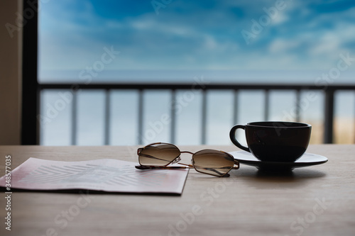 Breakfast in a Cafe on the Beach. White Coffee Cup on the Wooden Beach Table. cofee with sunglasses and news paper. beach background. holiday background. restaurant open. cafe coffee background