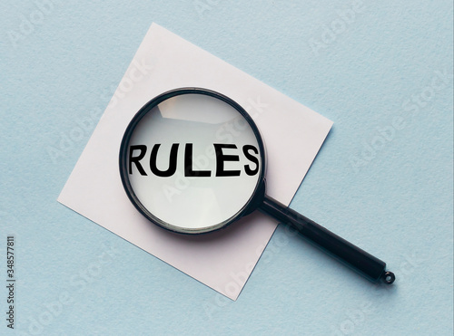 Magnifying glass or loupe with the word rules on a white memo note on blue background. Searching new rules photo
