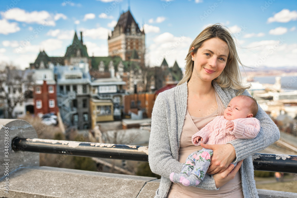 blonde women with baby at the blurred Frontenac Castle in the background, Quebec, Canada