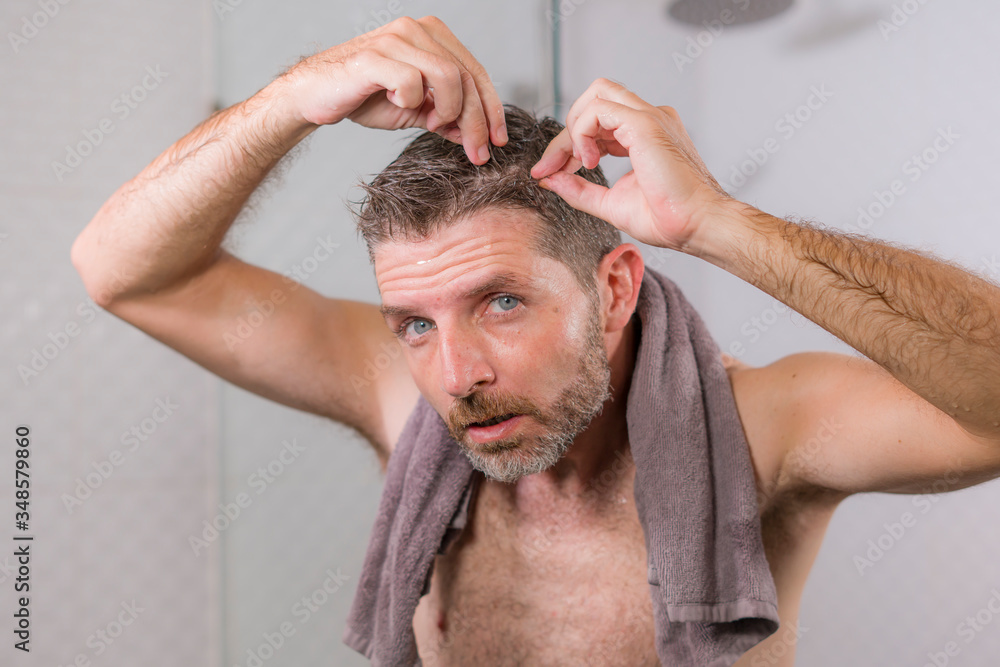 Obraz premium lifestyle portrait of mid adult attractive concerned and upset man at home bathroom searching and finding gray hair looking at the mirror worried about aging