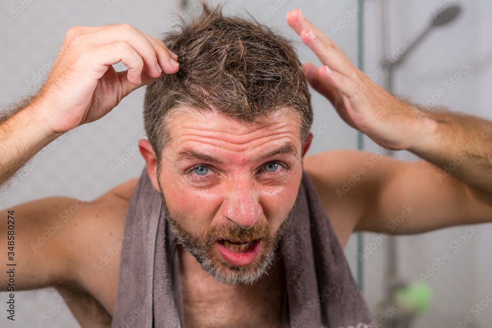 Obraz premium lifestyle portrait of mid adult attractive concerned and upset man at home bathroom searching and finding gray hair looking at the mirror worried about aging