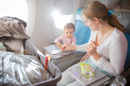 a little cute toddler girl sitting in an airplane in a chair at the porthole wipes with her mother a folding table with a wet antibacterial wipe before eating.