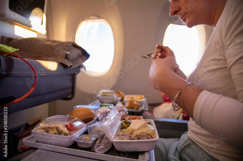  women passenger of aircraft seats in seat and  eats tasty hot inflight meal  on a folding table. in the background is a window in the porthole. side view photo