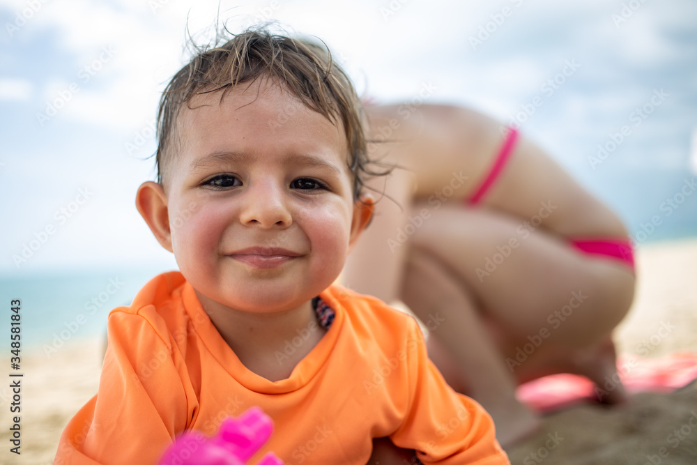 portrait of a little cute wet after bathing a happy and tired kid looking at the camera on the background of a sandy beach, pestilence and mom portrait of a little cute wet after bathing a happy and tired kid looking at the camera on the background of a sandy beach, pestilence and mom