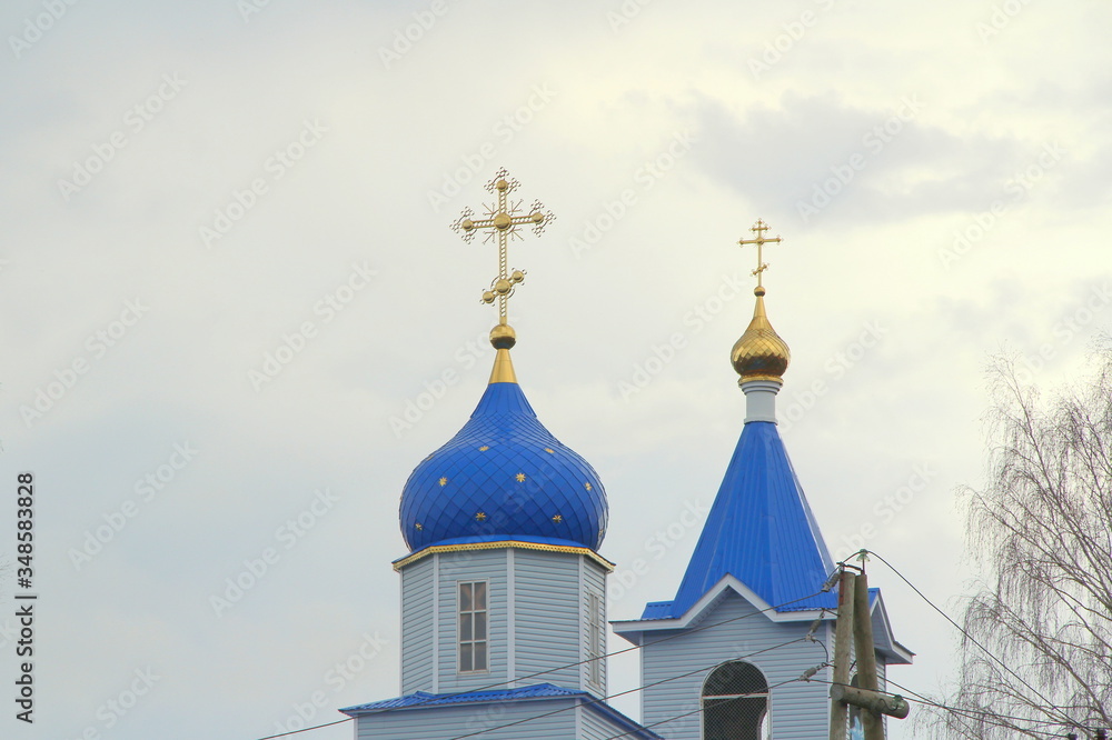 Orthodox Christian church with white walls, blue domes and golden crosses in Russia. A building for religious ceremonies with a bell tower against a cloudy sky in the countryside.
