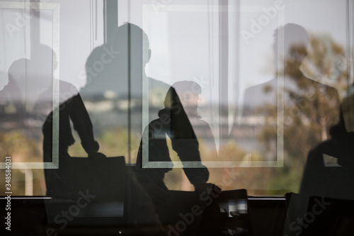 Sillohetted business people in meeting seen through glass wall with reflection