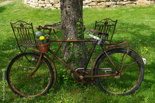 Altes verrostetes Fahrrad mit Blumen geschmückt an einen Baum gelehnt