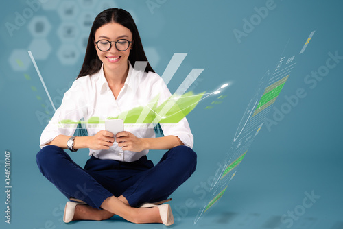 A beautiful young Asian woman is sitting on the floor with holographic graphcis floating around her and from her phone towards her, depicting a modern environments of analytics and big data. photo