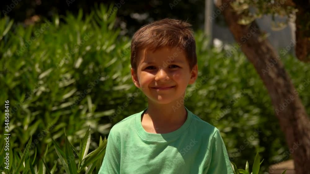 A happy boy in a green t-shirt smiles and shows his big thumb up and counts on the fingers outdoors