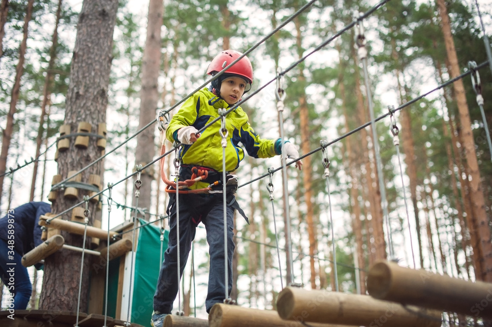 Boy climbing in an adventure park. In a green jacket and a red helmet. Overcomes obstacles. Boy climbing in an adventure park. In a green jacket and a red helmet. Overcomes obstacles.