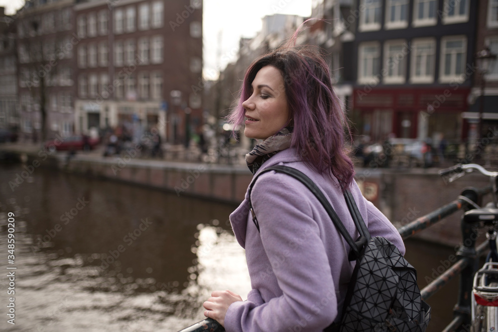 Girl in the coat and backpack enjoying city. Young woman looking to the side on Amsterdam channel, Netherlands