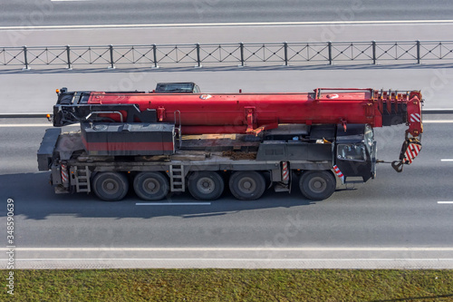 Heavy red mobile crane with folding boom construction rides on a city highway.