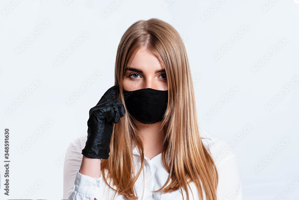 Doctor in a white suit and medical mask, holding hands in black gloves and thinking about the consequences of the coronavirus epidemic. Doctor on a white background. The doctor puts on a black mask. Doctor in a white suit and medical mask, holding hands in black gloves and thinking about the consequences of the coronavirus epidemic. Doctor on a white background. The doctor puts on a black mask.