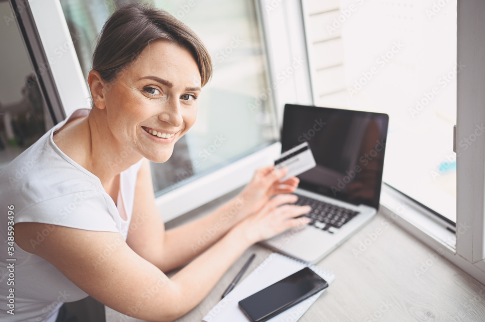 Beautiful happy woman holding credit card in hand and using laptop computer keyboard. Businesswoman or entrepreneur working. Online shopping, e-commerce, internet banking, spending money concept Beautiful happy woman holding credit card in hand and using laptop computer keyboard. Businesswoman or entrepreneur working. Online shopping, e-commerce, internet banking, spending money concept