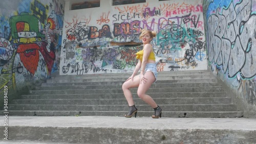 The girl is dancing kizomba. Sexy funny woman dancing african dance on graffiti background. Beautiful young dancer seductively dances and moves her buttocks. Graffiti, skate park. photo