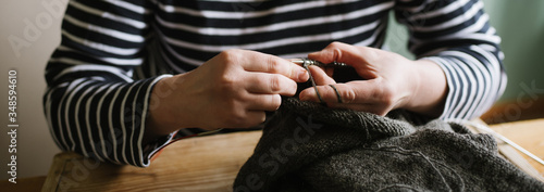 Close up photo of woman's hands knitting on grey yarn on wooden © Liliia Mykhalevych