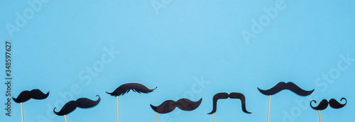 Various black photo booth props moustaches of different shape on blue background. Greeting card for father's day or men's health awareness month campaign concept. Flat lay, banner