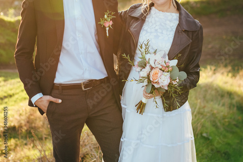 The bride and groom stand at sunset and hold hands.