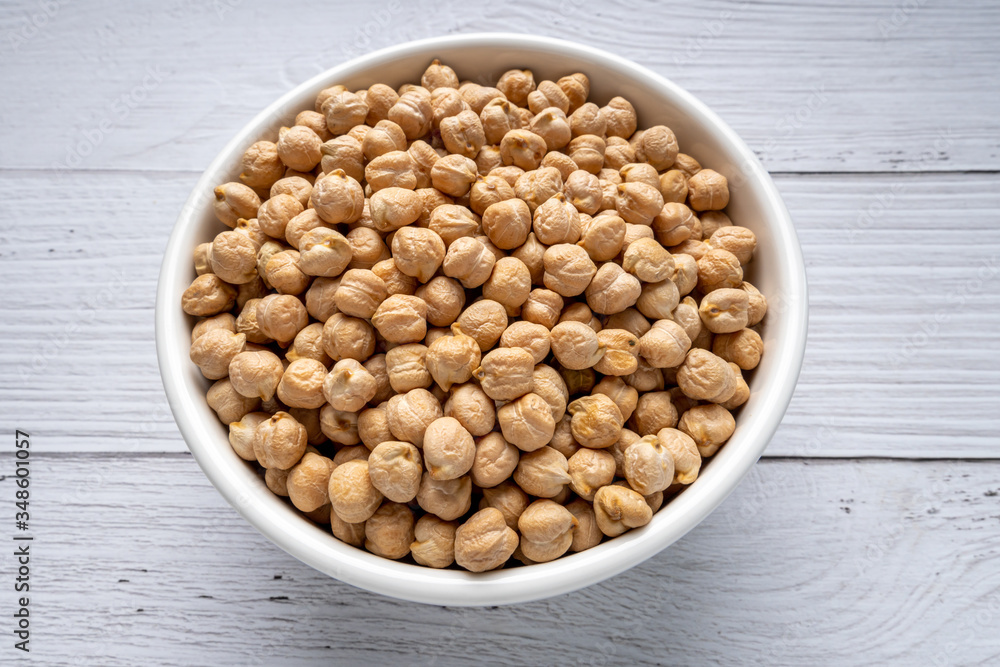Uncooked dried chickpeas in bowl on white wooden table. Heap of legume chickpea background. top view. vegan food concept Uncooked dried chickpeas in bowl on white wooden table. Heap of legume chickpea background. top view. vegan food concept
