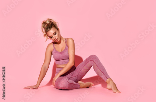 Young active girl in fashionable rose sportswear sitting on floor looking down tired of trainings. Full length portrait isolated on white, copy space