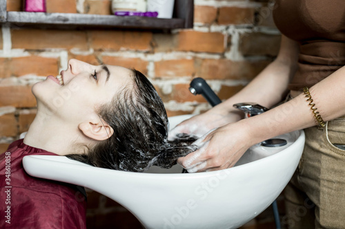 Washing hair in a beauty salon in the sink before cutting, close-up. The Barber washes the client's hair in the sink with professional shampoo. Hair care. Hairdressing services.