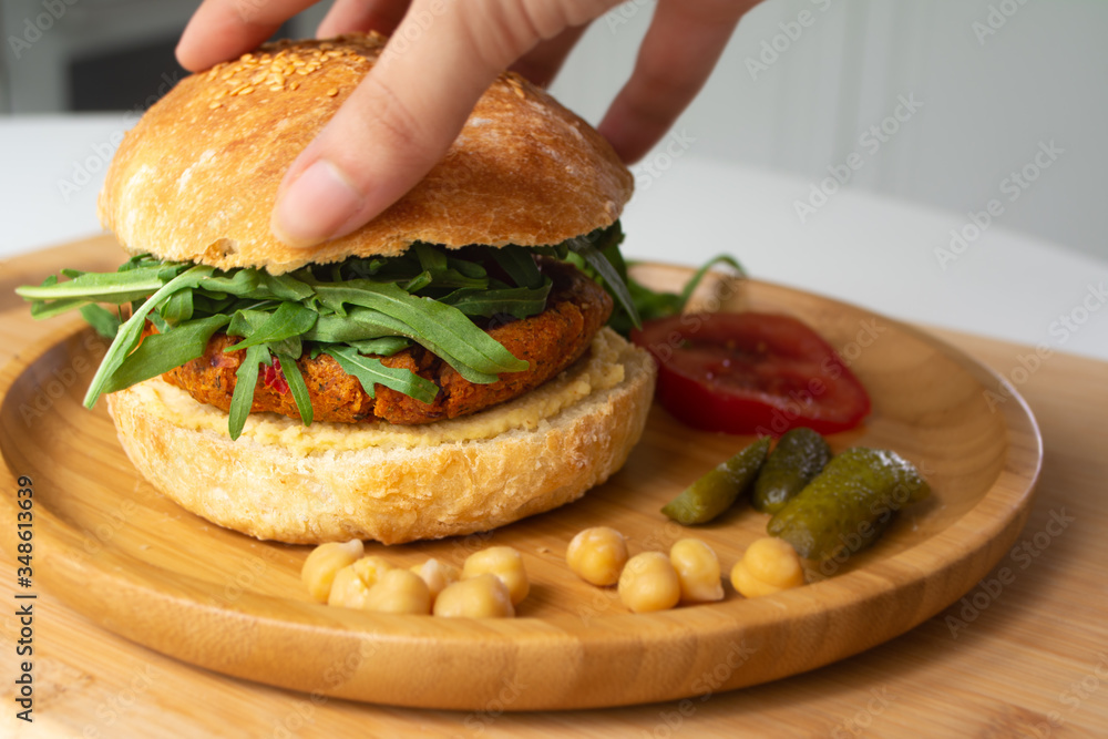 Vegan falafel hummus burger with homemade sourdough bun, tomatoes, pickled cucumbers and arugula in a wooden plate Vegan falafel hummus burger with homemade sourdough bun, tomatoes, pickled cucumbers and arugula in a wooden plate