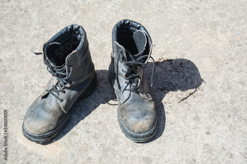 Pair of old used work boots on concrete background. Dirty black leather boots from the army.