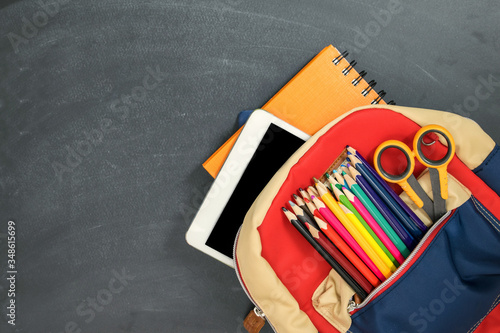 Back to school concept. Backpack with school supplies, tablet and against chalk board. Top view. Copy space