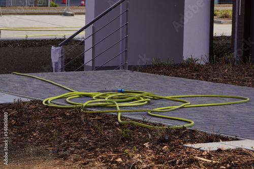Yellow-green watering hose on the sidewalk, watering plants in the garden, vegetable garden or on the lawn of an apartment building