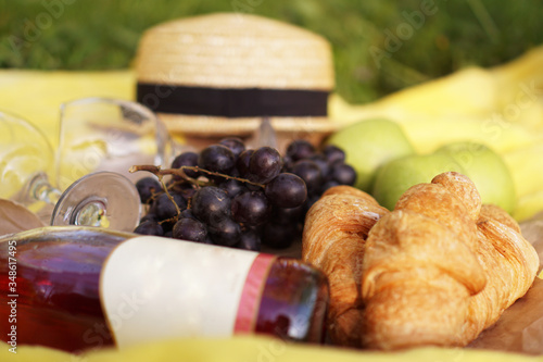 Picnic on the grass with croissant, pink wine, straw hat, grape on yellow plaid and green grass. Summer time