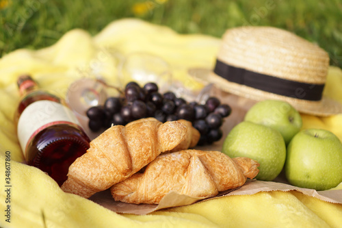 Picnic on the grass with croissant, pink wine, straw hat, grape on yellow plaid and green grass. Summer time
