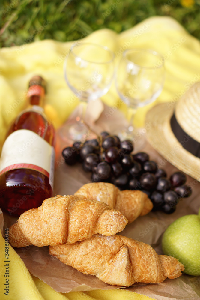 Picnic on the grass with croissant, pink wine, straw hat, grape on yellow plaid and green grass. Summer time - vertical photo Picnic on the grass with croissant, pink wine, straw hat, grape on yellow plaid and green grass. Summer time - vertical photo