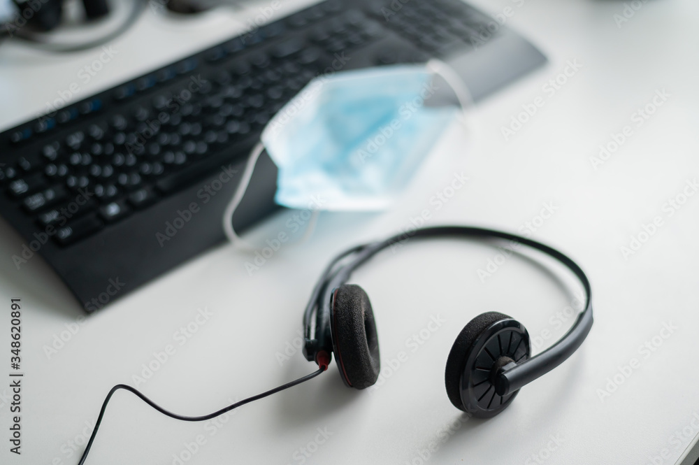 Headset and medical mask near the keyboard on the desktop of a call center operator in the office. The concept of safe operation during the coronavirus epidemic. Headset and medical mask near the keyboard on the desktop of a call center operator in the office. The concept of safe operation during the coronavirus epidemic.