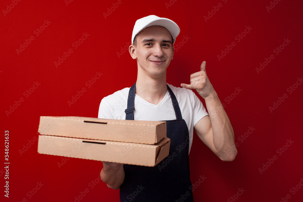 food delivery man holds packaging and shows a call gesture, the courier holds an order and calls on a red background food delivery man holds packaging and shows a call gesture, the courier holds an order and calls on a red background