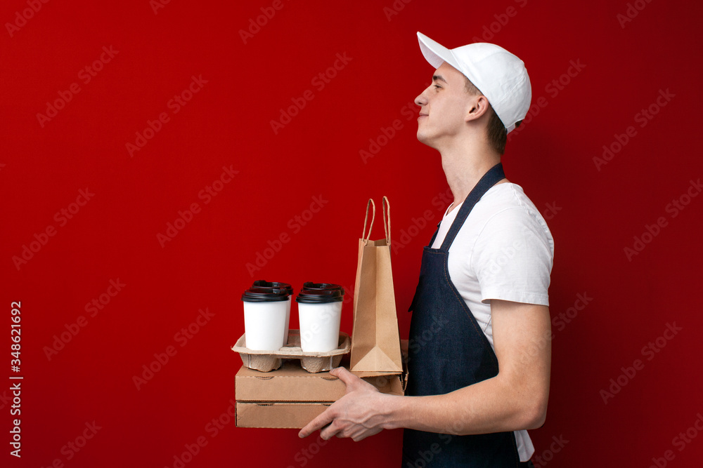 young positive food delivery man on red background, courier guy holds a lot of packaging and smiles young positive food delivery man on red background, courier guy holds a lot of packaging and smiles