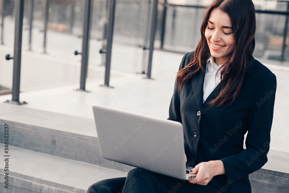 Successful smiling businesswoman or entrepreneur using laptop sitting in front of his office. Successful smiling businesswoman or entrepreneur using laptop sitting in front of his office.