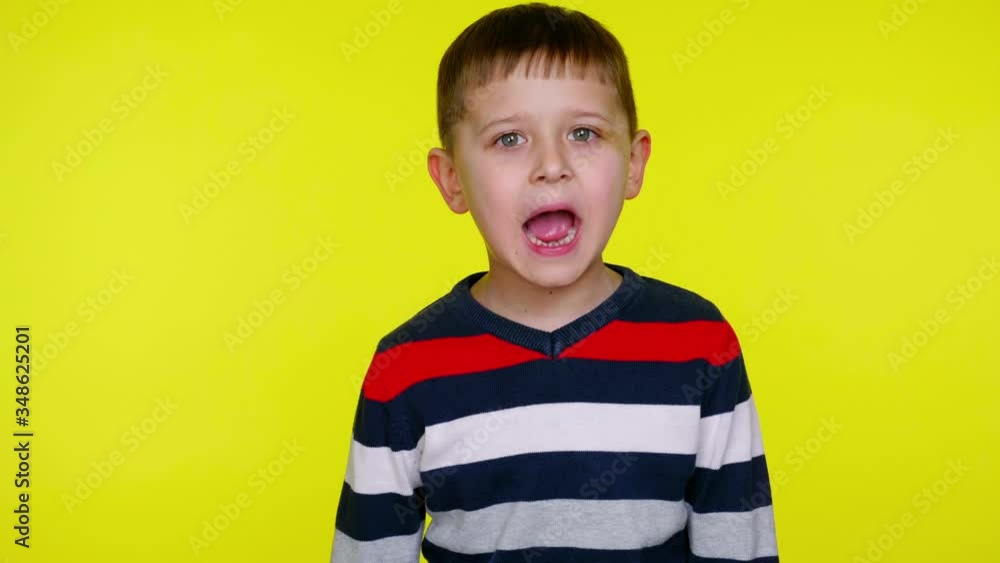 Little child boy in a colorful sweater screaming on a yellow background with copy space. Place for text or product. 4K slowmotion footage Little child boy in a colorful sweater screaming on a yellow background with copy space. Place for text or product. 4K slowmotion footage