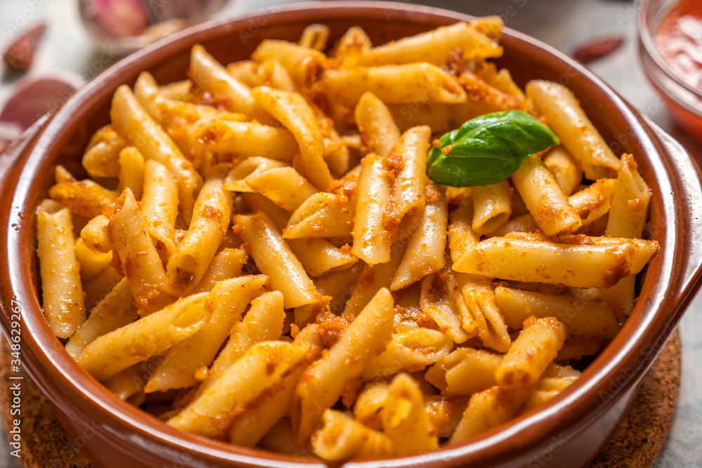 Macarrones con pesto rojo y una hoja de albahaca fresca en una cazuela de barro Macarrones con pesto rojo y una hoja de albahaca fresca en una cazuela de barro