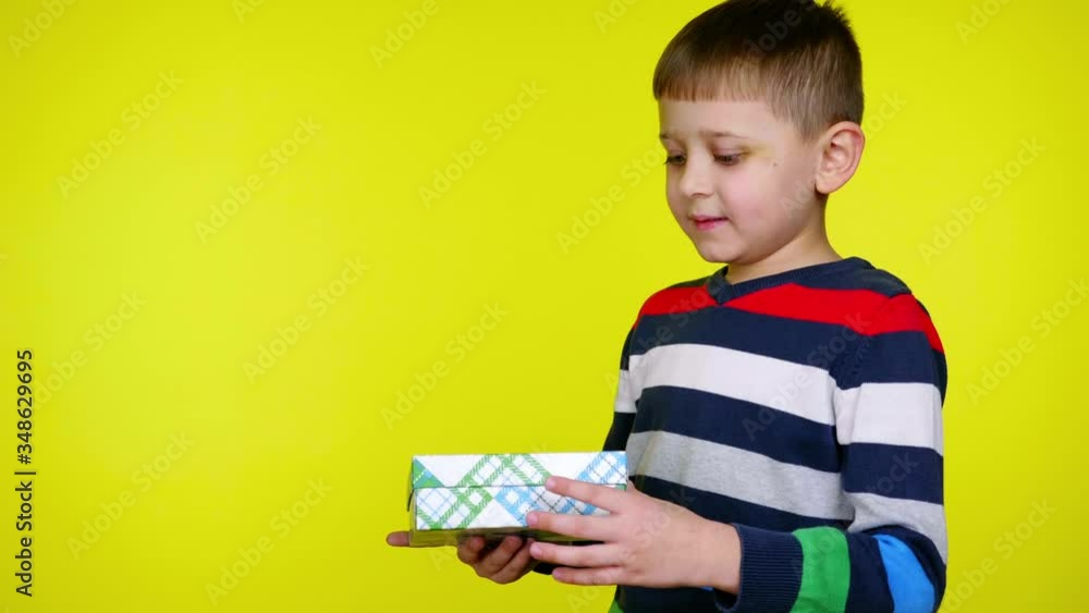 Happy little child boy in a multi-colored sweater takes box with gift in his hands, opens and is surprised on yellow background with copy space. Place for text or product. 4K slowmotion footage Happy little child boy in a multi-colored sweater takes box with gift in his hands, opens and is surprised on yellow background with copy space. Place for text or product. 4K slowmotion footage