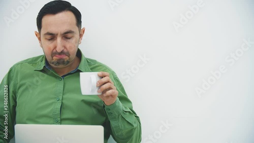 Isolated serious young man sitting on the floor with laptop on his knees, searching in the internet, drinking strong coffee. photo