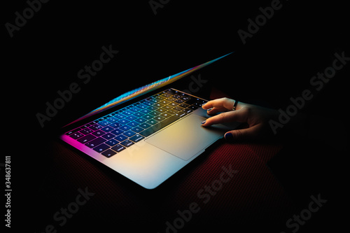 Modern laptop with colored lights on the screen that illuminate the keyboard with one hand on the laptop