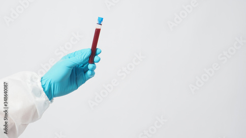 Male model with PPE suite and Hand with glove is holding blood test tube on white background.