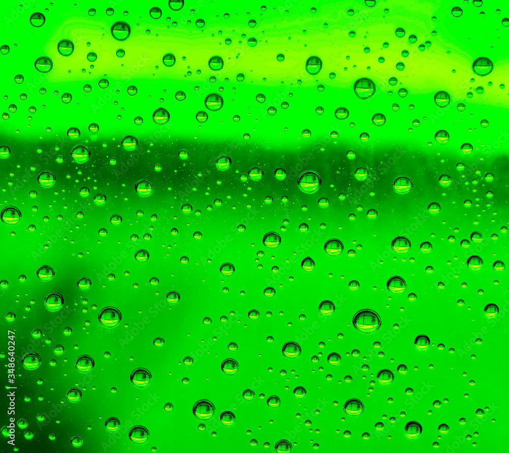 green rain water drops on a window glass close up , colored drop background macro in a green light