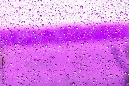 violet rain water drops on a window glass close up , purple colored drop macro in a crimson light