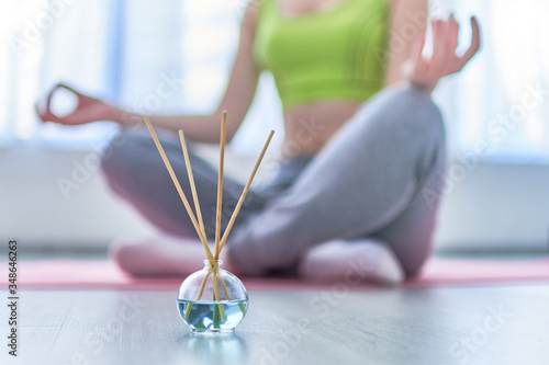 Fitness woman in lotus pose with aroma sticks and essential oil bottle during yoga training, aromatherapy treatments and meditation. Mental health photo