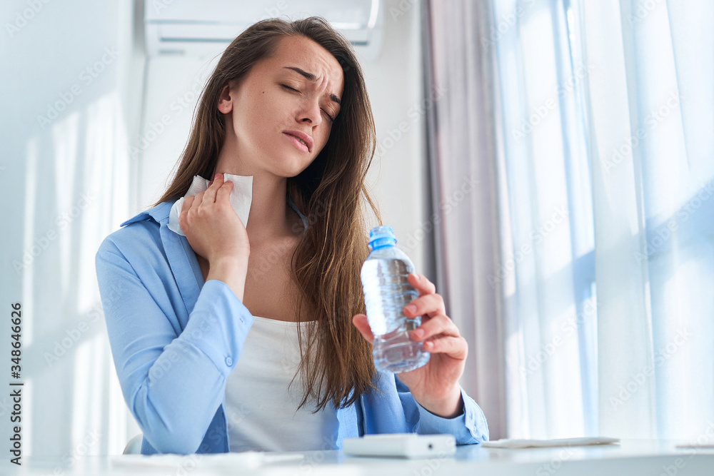 Sweating woman suffering from heat, hot weather and thirst wipes his neck with a napkin and cools down with cold refreshing water bottle. Refresh concept Sweating woman suffering from heat, hot weather and thirst wipes his neck with a napkin and cools down with cold refreshing water bottle. Refresh concept
