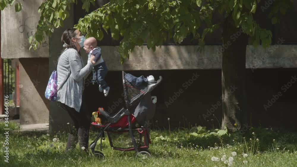 Mother wearing a protective mask on the face while taking care of a newborn baby boy during COVID-19 pandemic, quarantine outdoor life, free time. Mother wearing a protective mask on the face while taking care of a newborn baby boy during COVID-19 pandemic, quarantine outdoor life, free time.