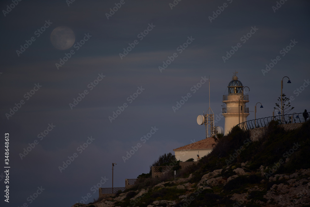 Moon eclipse over a lighthouse on the coast